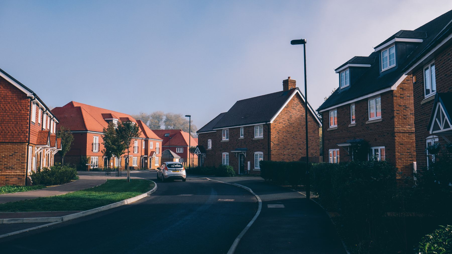 A quiet English residential street of red-brick houses in warm morning light